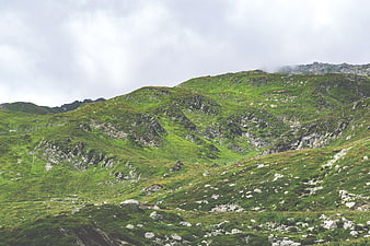 Lush green mountain landscape with rocky slopes and cloudy sky
