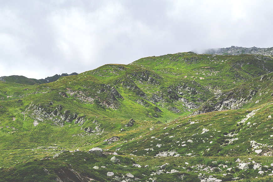 Lush green mountain landscape with rocky slopes and cloudy sky