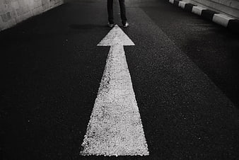 Black and white arrow on asphalt road pointing forward