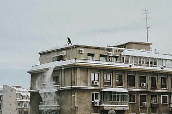 Man clearing snow from apartment building rooftop in winter