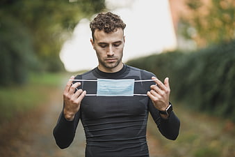 Athletic man holding medical mask outdoors