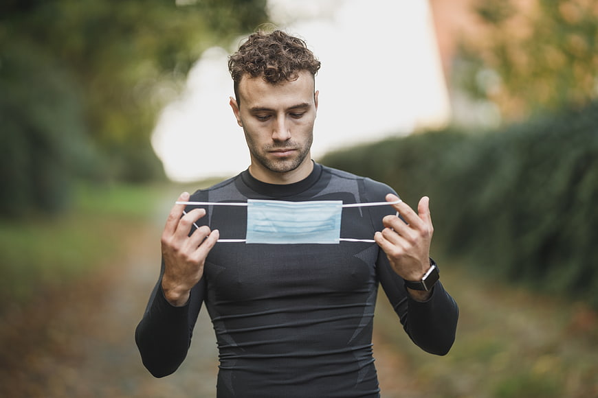 Athletic man holding medical mask outdoors