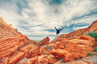 Woman jumping joyfully on red rock formation under dramatic sky