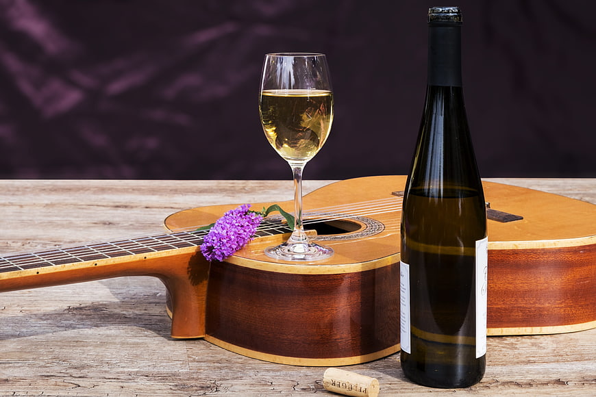 Acoustic Guitar with White Wine and Purple Flowers on Wooden Table