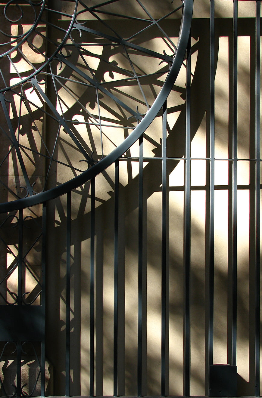 Abstract shadows of wrought iron gate on beige wall