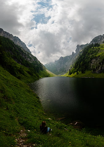 Woman sitting by alpine lake in mountain valley