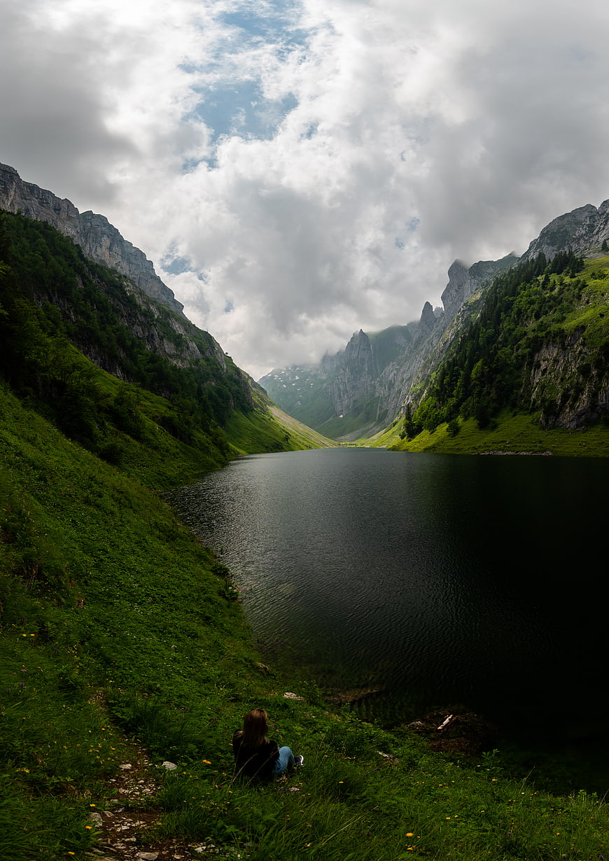 Woman sitting by alpine lake in mountain valley
