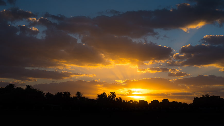 Dramatic sunset with sun rays breaking through clouds over silhouette