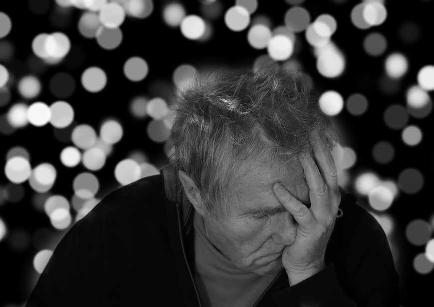 Senior man in despair with hand on forehead against bokeh background