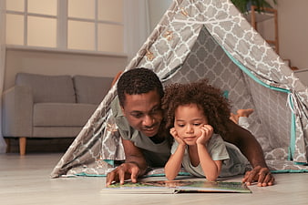 Father and daughter reading book in play tent at home