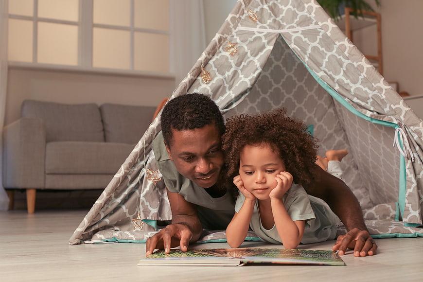 Father and daughter reading book in play tent at home