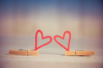 Two wooden clothespins holding red heart cutouts on a blurred background
