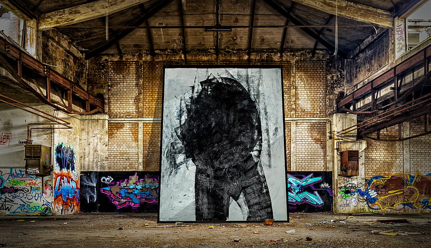 Large black and white portrait painting in abandoned industrial factory