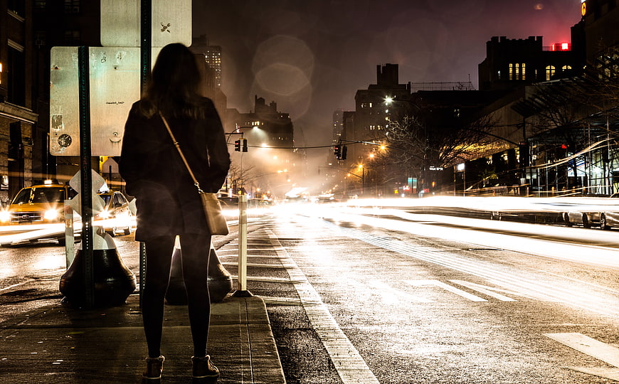 Woman waiting at city bus stop at night with light trails
