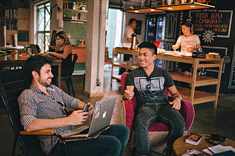 Two happy men talking and working with laptop in cafe