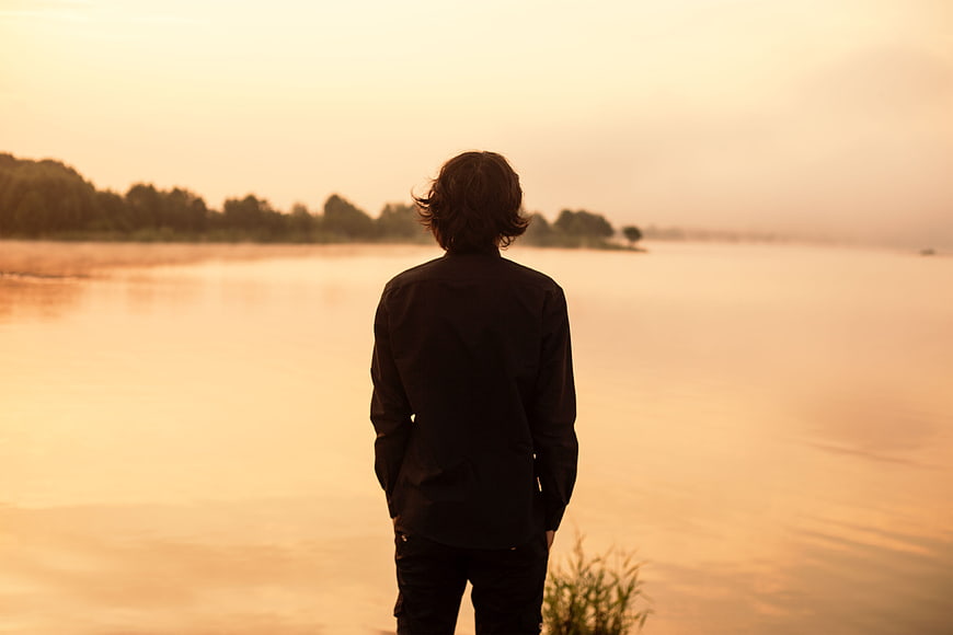 Man Standing by Lake at Sunset Looking at Horizon