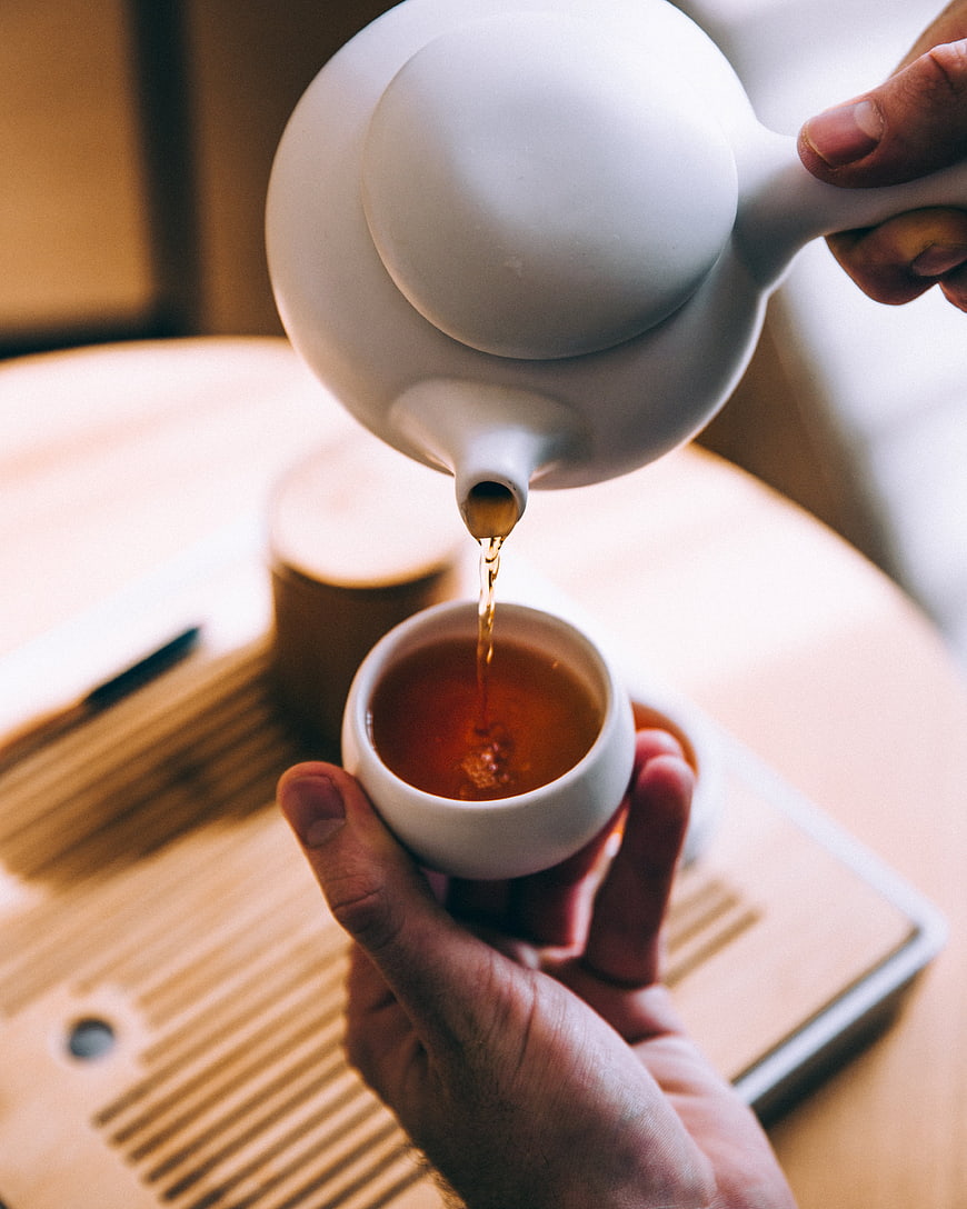 Hands Pouring Tea from White Teapot into Cup
