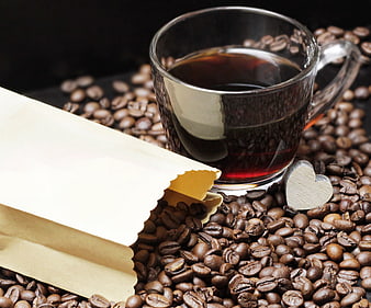 Glass cup of black coffee with roasted beans and paper bag