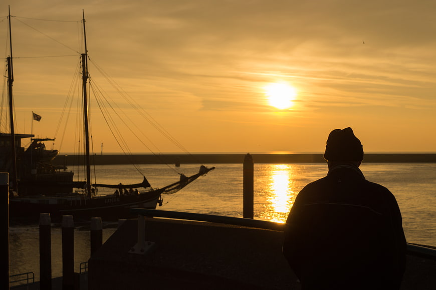 Silhouette of man watching golden sunset over harbor with boat