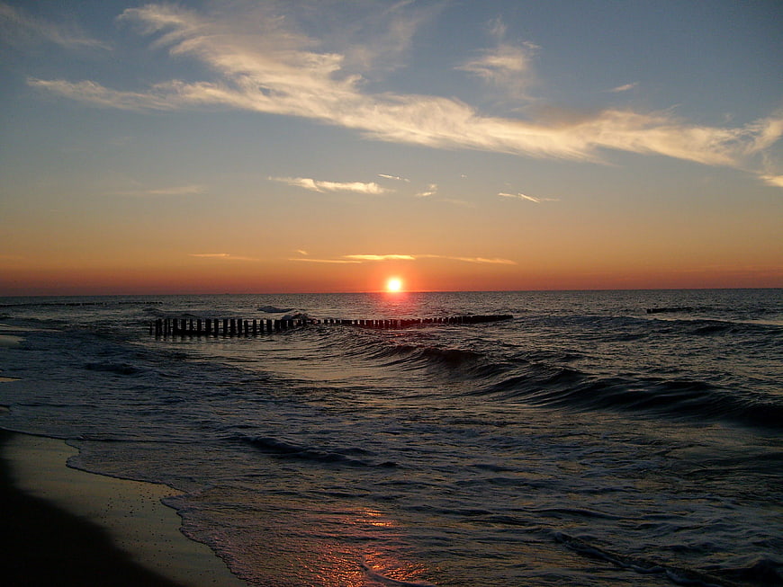 Sunset over ocean with wooden groynes and waves