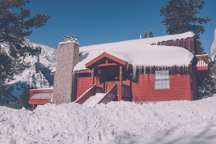 Red wooden cabin covered in snow and icicles in winter mountains