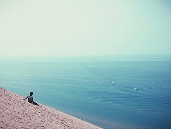 Man Sitting on Pink Sand Dune Overlooking Calm Ocean