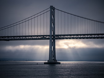 Dramatic suspension bridge over ocean with sun rays through clouds