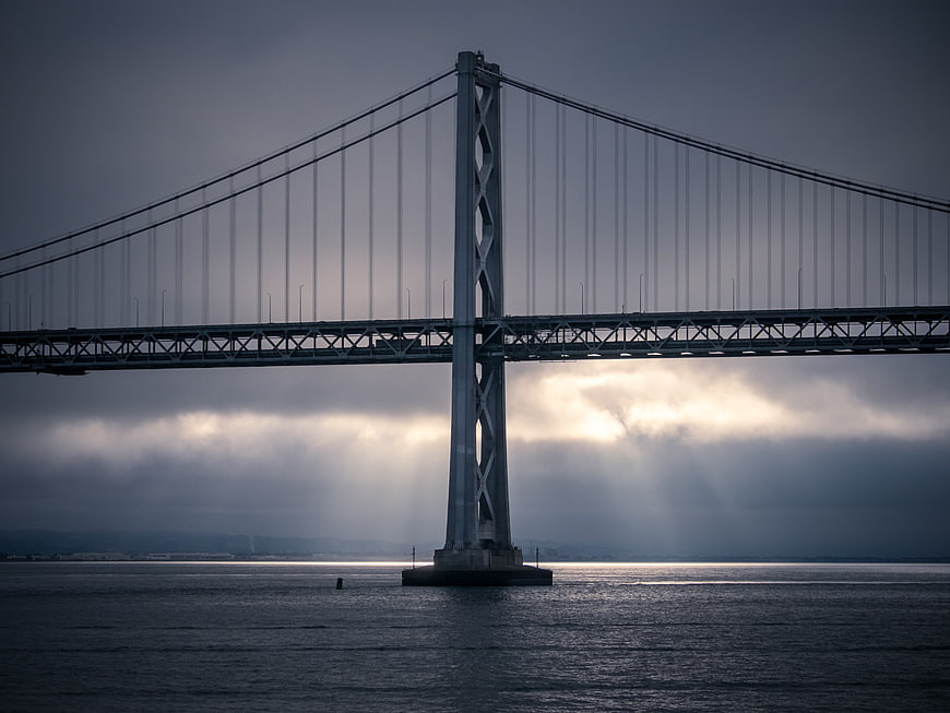 Dramatic suspension bridge over ocean with sun rays through clouds