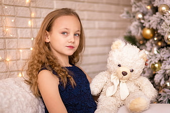 Young girl holding white teddy bear near Christmas tree