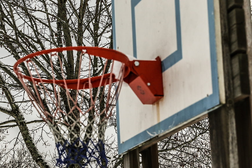 Outdoor basketball hoop with red rim and net against bare trees