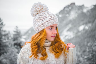 Redhead woman in white knit hat and sweater in snowy mountains