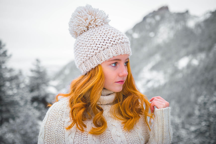 Redhead woman in white knit hat and sweater in snowy mountains