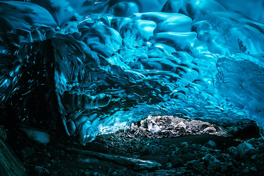 Glowing Blue Ice Cave Interior with Rocky Floor