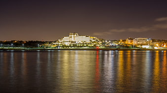 Night view of illuminated coastal resort city skyline with water reflections