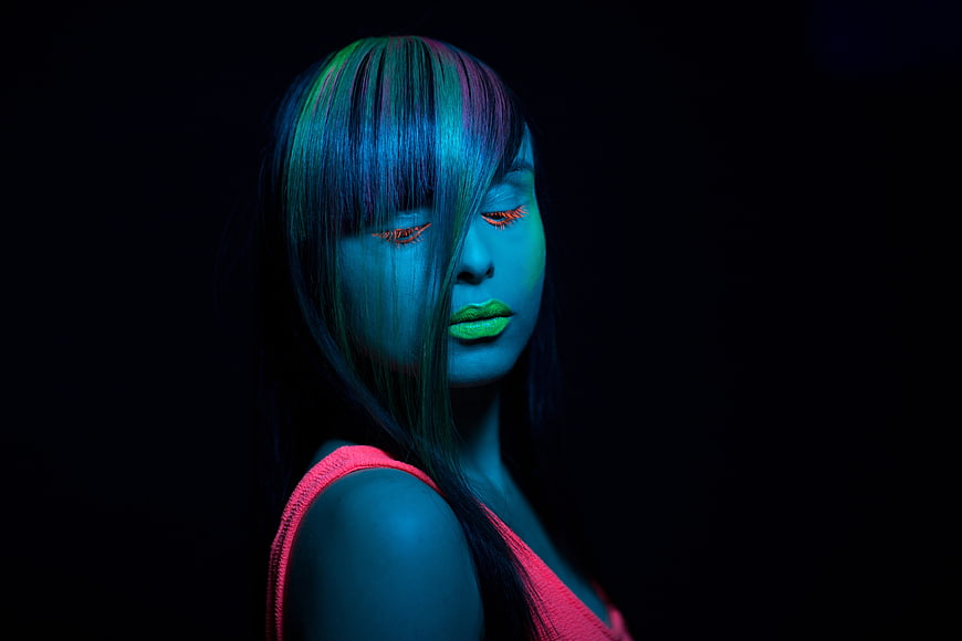 Woman with neon makeup and blue lighting in dark studio