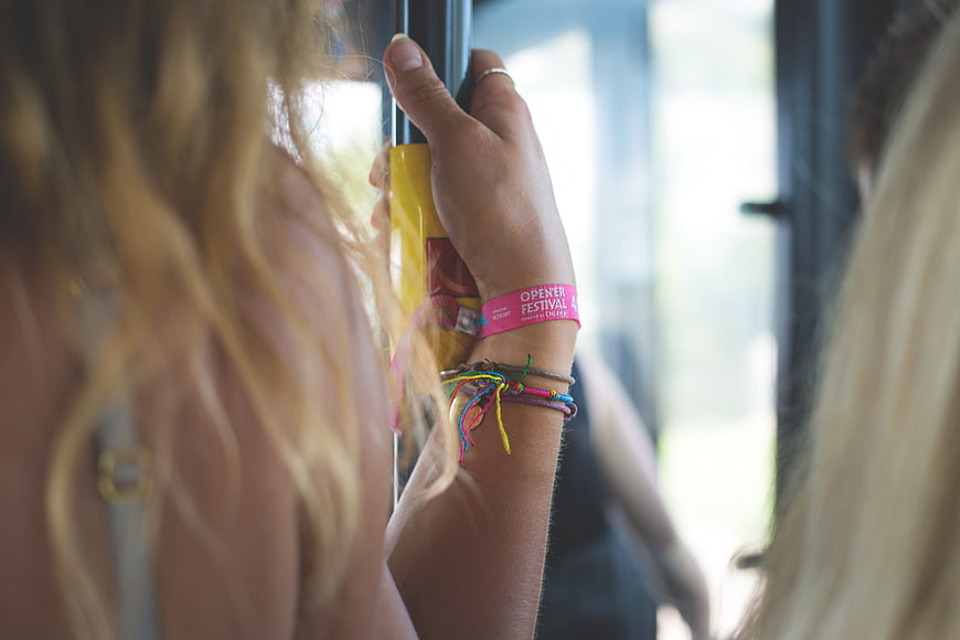 Close-up of hand holding bus pole with festival wristband