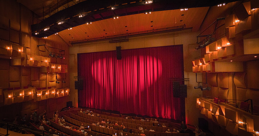 Interior of a modern theater with red curtain and audience