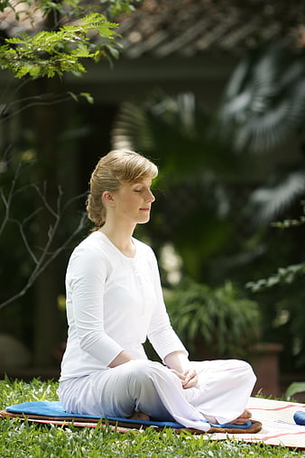 Woman meditating in lotus position on blue cushion in garden