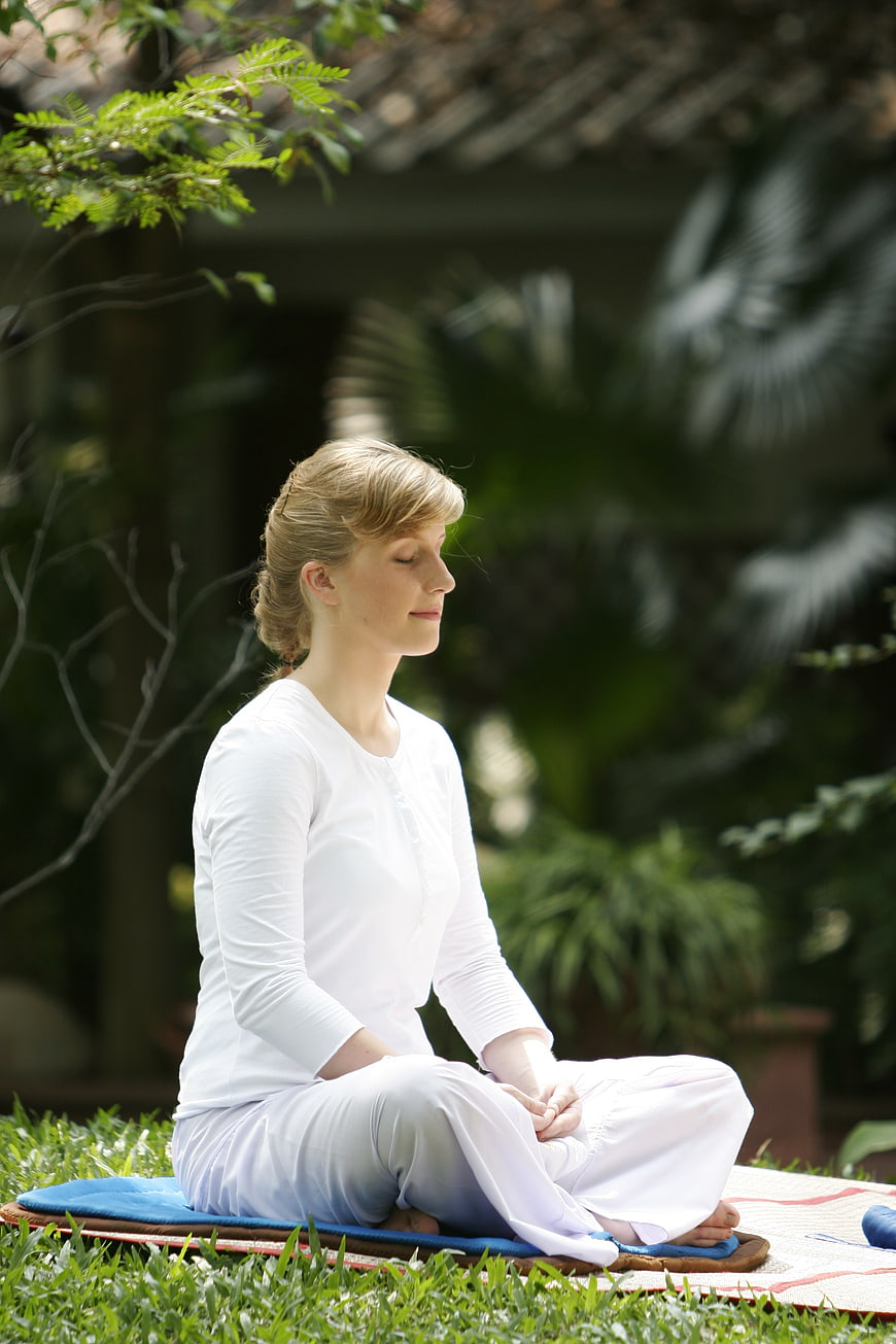 Woman meditating in lotus position on blue cushion in garden