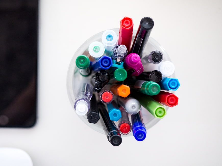 Top View of Colorful Markers in Clear Cup on White Desk