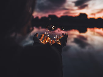 Woman holding fairy lights against sunset sky reflection