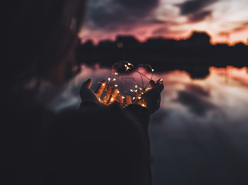 Woman holding fairy lights against sunset sky reflection