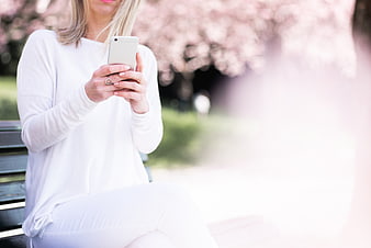 Woman using smartphone on park bench with cherry blossoms