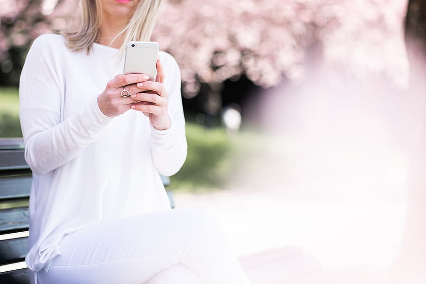 Woman using smartphone on park bench with cherry blossoms