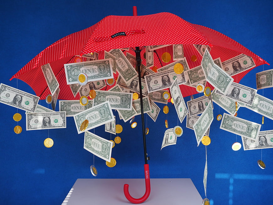 Red Umbrella Protecting Dollar Bills and Coins Against Blue Background