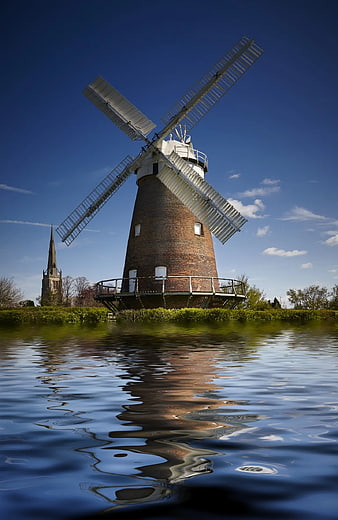 Traditional Brick Windmill Reflected in Water Under Blue Sky