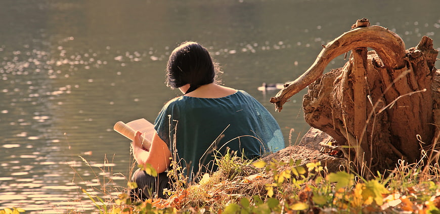 Woman reading a book by a lake in autumn