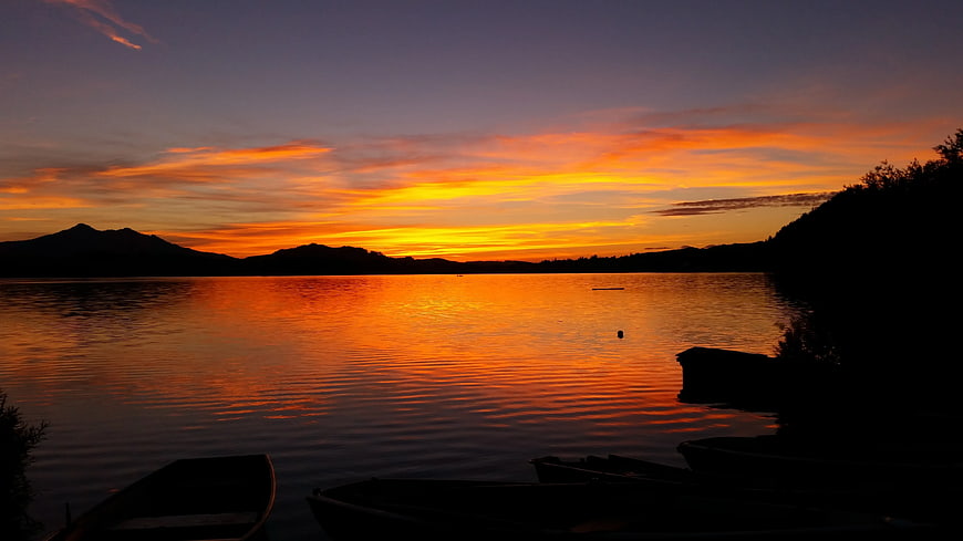 Vibrant orange sunset over calm lake with silhouetted boats