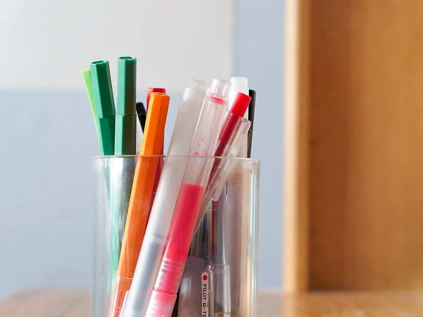 Colorful pens and markers in a clear glass cup on a desk