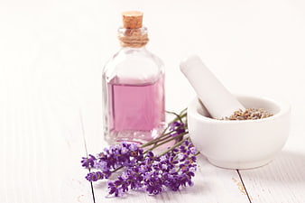 Lavender essential oil bottle with mortar and pestle on white wood